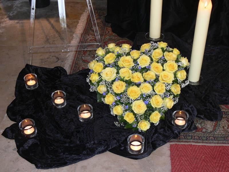 Ein herzförmiges Arrangement aus gelben Rosen ist von Kerzen umgeben
