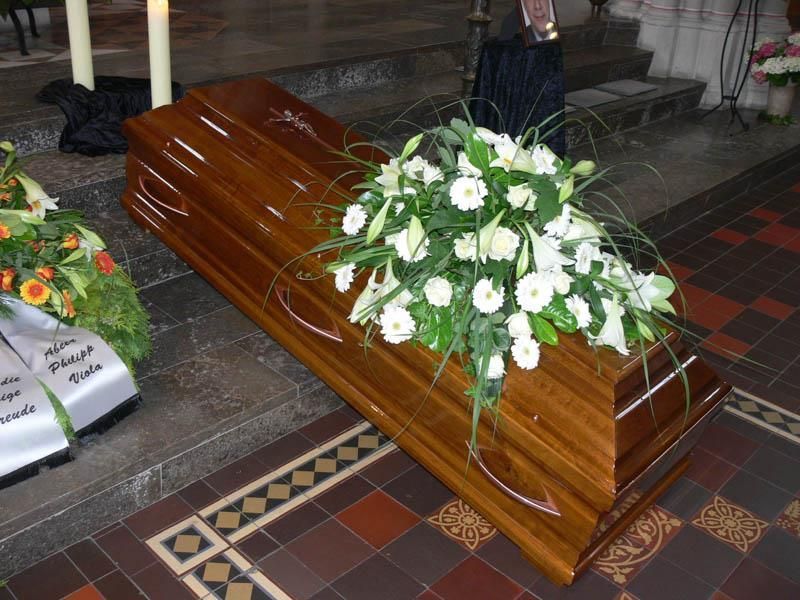 Ein Holzsarg ist in einer Kirche mit weißen Blumen geschmückt