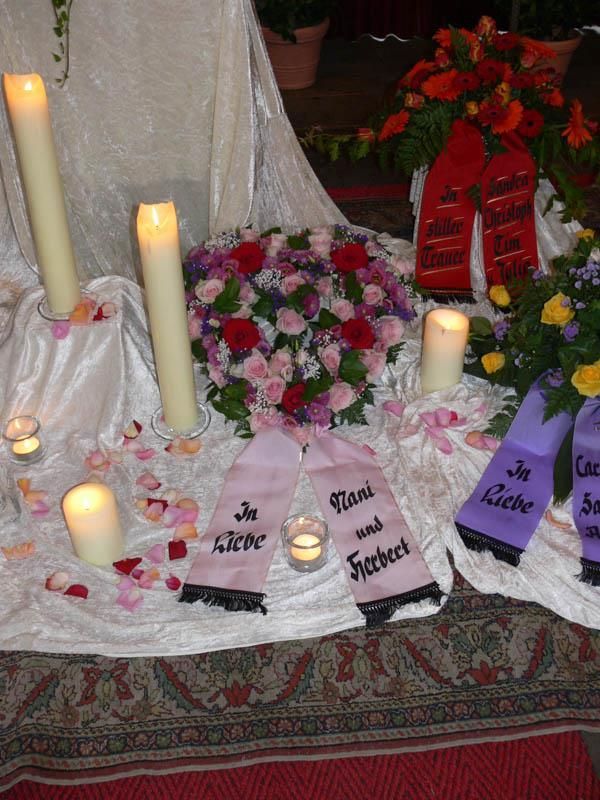 Eine Anordnung von Blumen und Kerzen mit einem lila Band, auf dem 