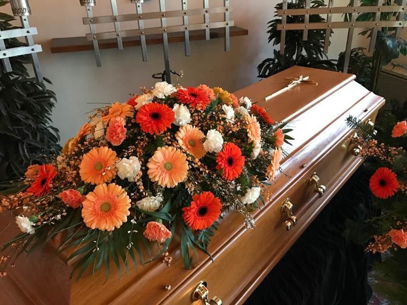 Ein Sarg ist mit orangen und weißen Blumen geschmückt
