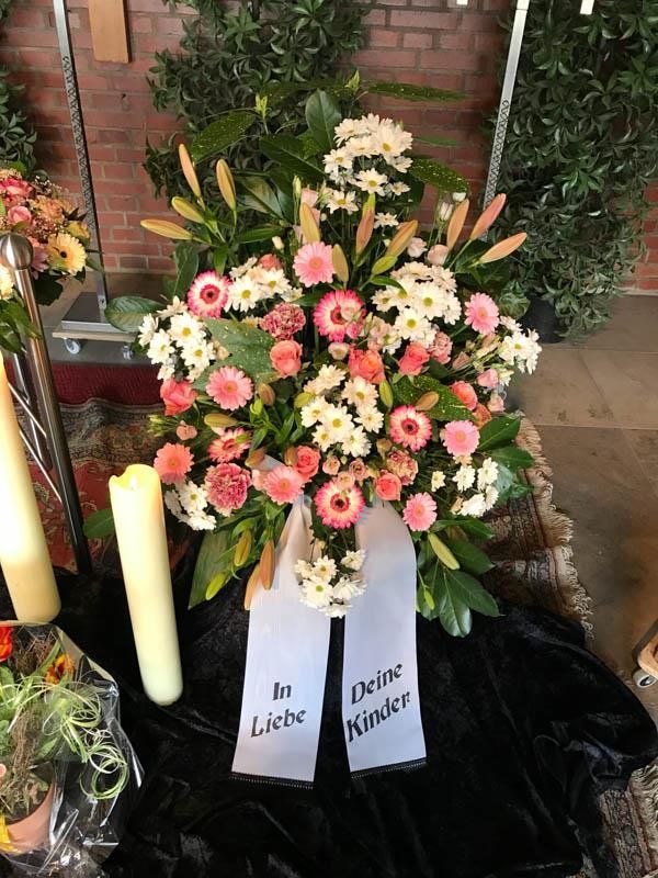 Ein Kranz aus rosa und weißen Blumen mit einer Schleife mit der Aufschrift „in Liebe“