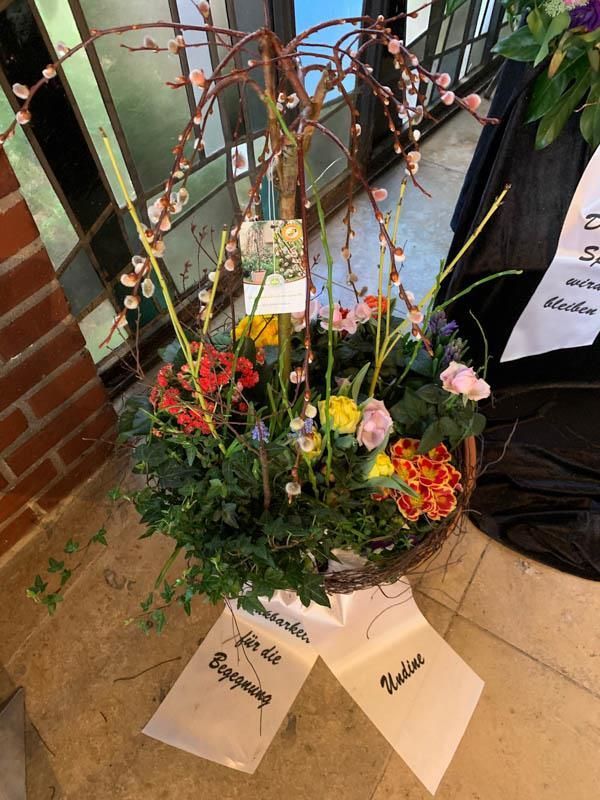 Ein Korb mit Blumen steht auf dem Boden neben einer Backsteinmauer