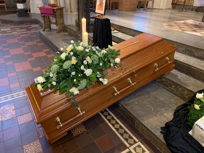 Ein Holzsarg mit Blumen und einer Kerze in einer Kirche.
