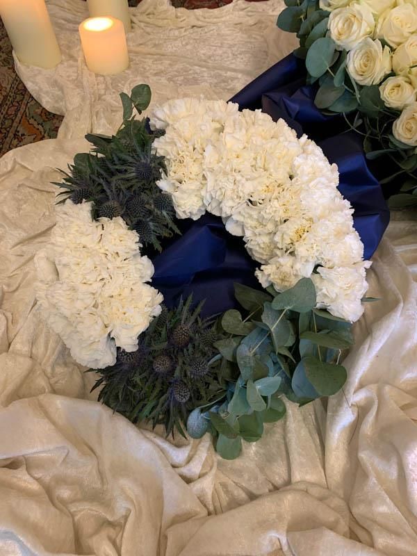 Auf einem Tisch steht ein Kranz aus weißen Blumen und Grünpflanzen.