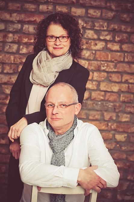Ein Mann und eine Frau posieren vor einer Backsteinmauer für ein Foto.