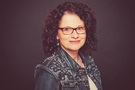 Eine Frau mit Brille und Jeansjacke lächelt in die Kamera.