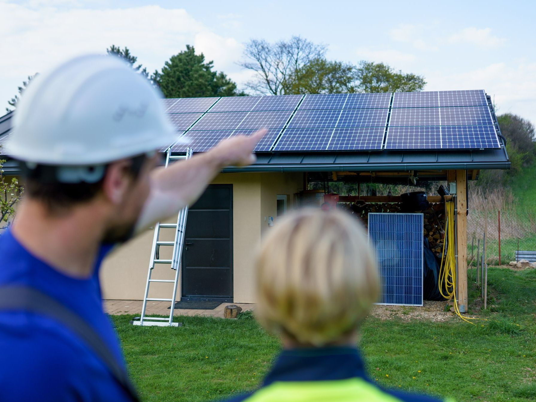 Installateur en train de pointer du doigt des panneaux solaires sur le toit d'une dépendance