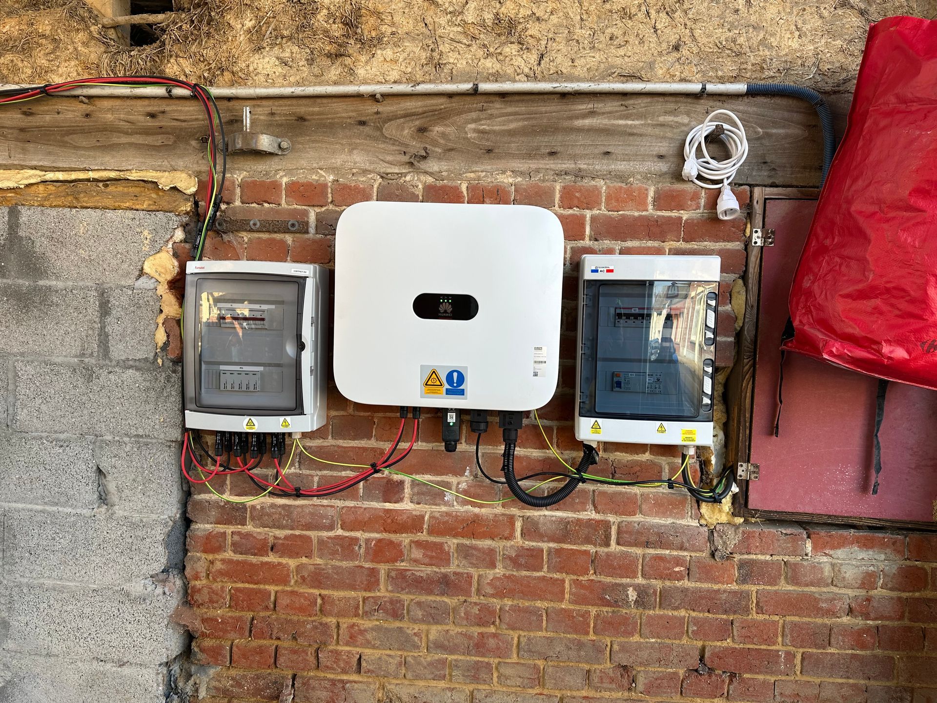 Câbles électriques branchés à une boîte blanche sur un mur de briques rouges