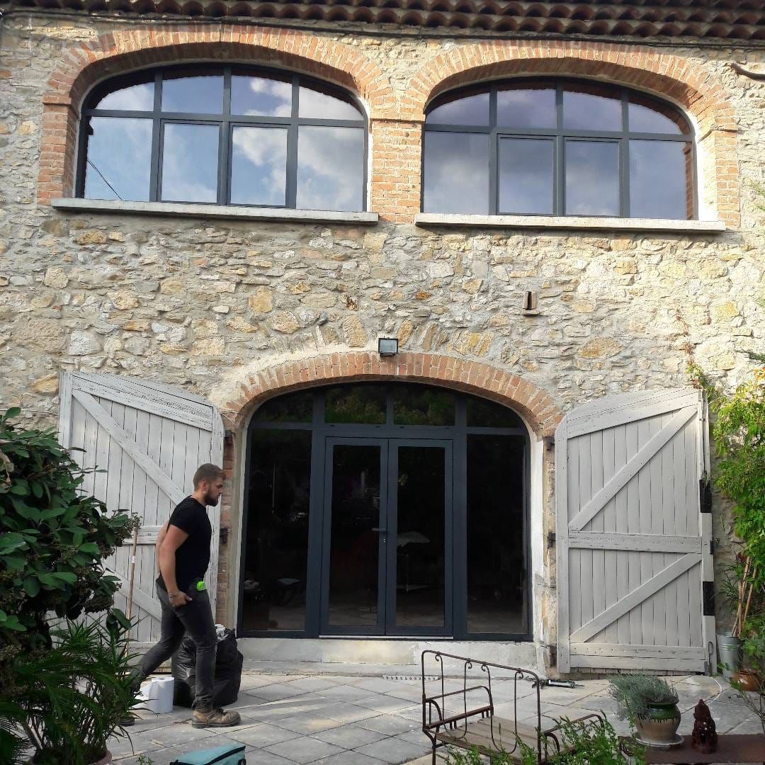 Un bâtiment en pierre, avec deux fenêtres cintrées à l'étage supérieur et une grande au rez-de-chaussée.