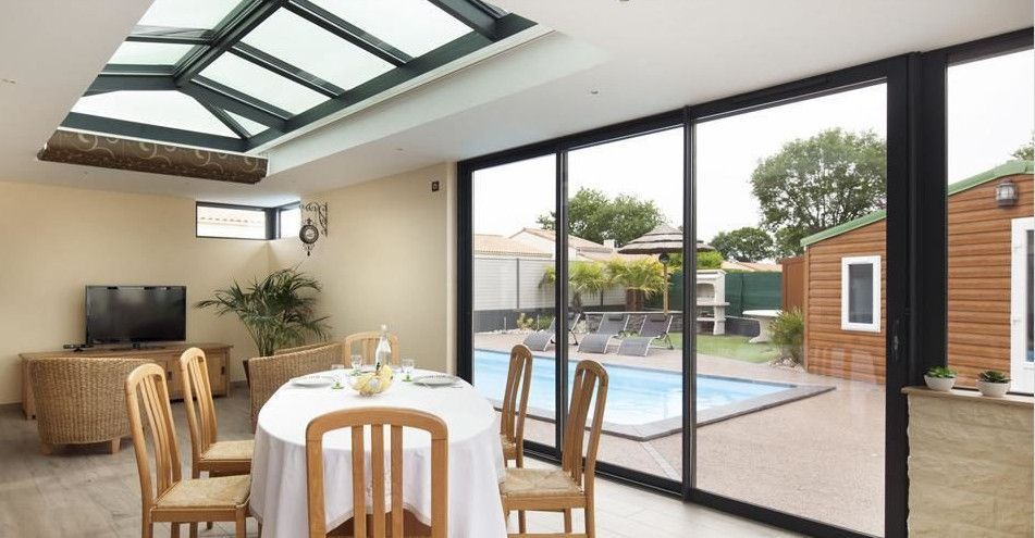 Salle à manger avec table, chaises et télévision, s'ouvrant par de grandes portes vitrées.