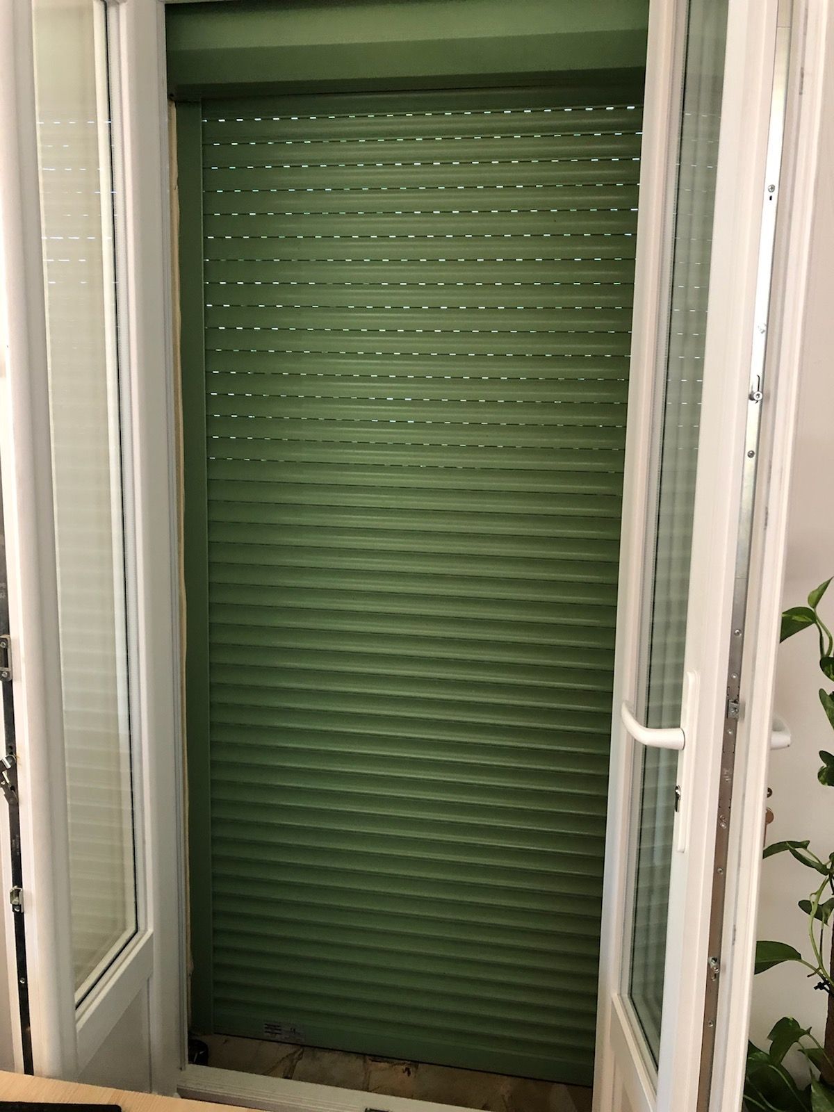 Un volet roulant vert est partiellement fermé sur une porte vitrée.