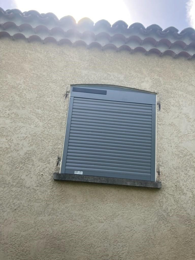 Un volet roulant gris foncé fermé, recouvrant une fenêtre.