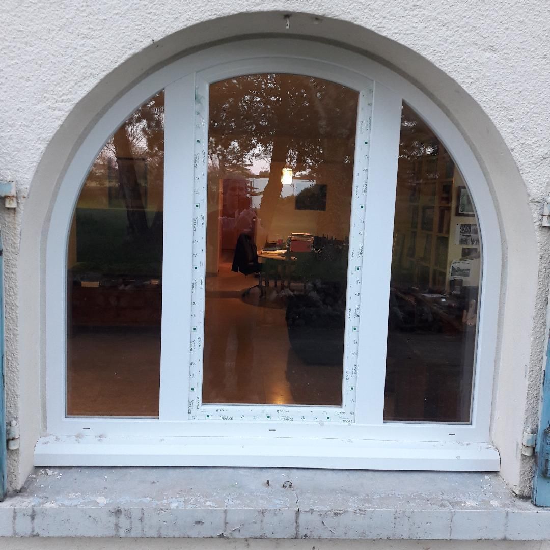 Une fenêtre blanche cintrée à trois carreaux de verre verticaux, encastrée dans un mur clair.