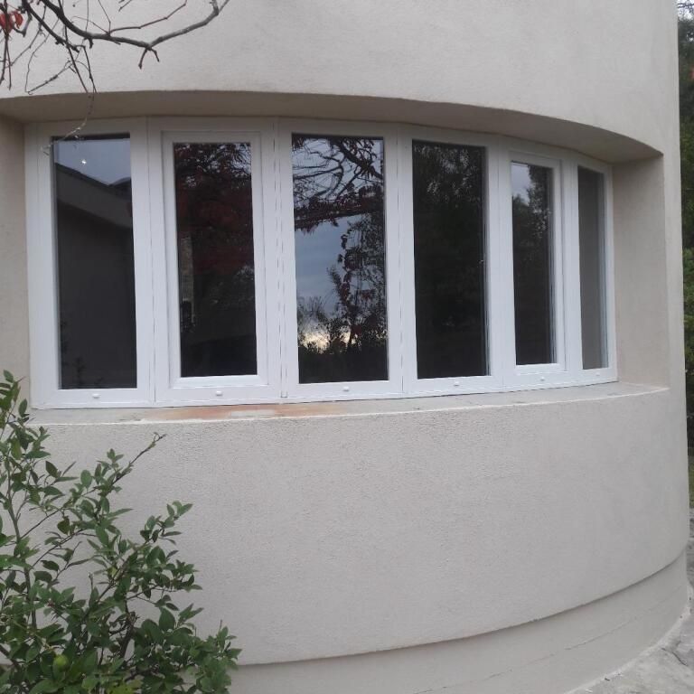 Une large fenêtre incurvée à cadre blanc, encastrée dans un mur extérieur beige.