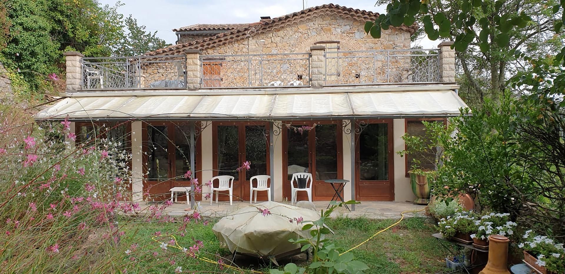 Une maison en pierre de deux étages avec un balcon, un auvent blanc des portes vitrées du rez-de-chaussée.
