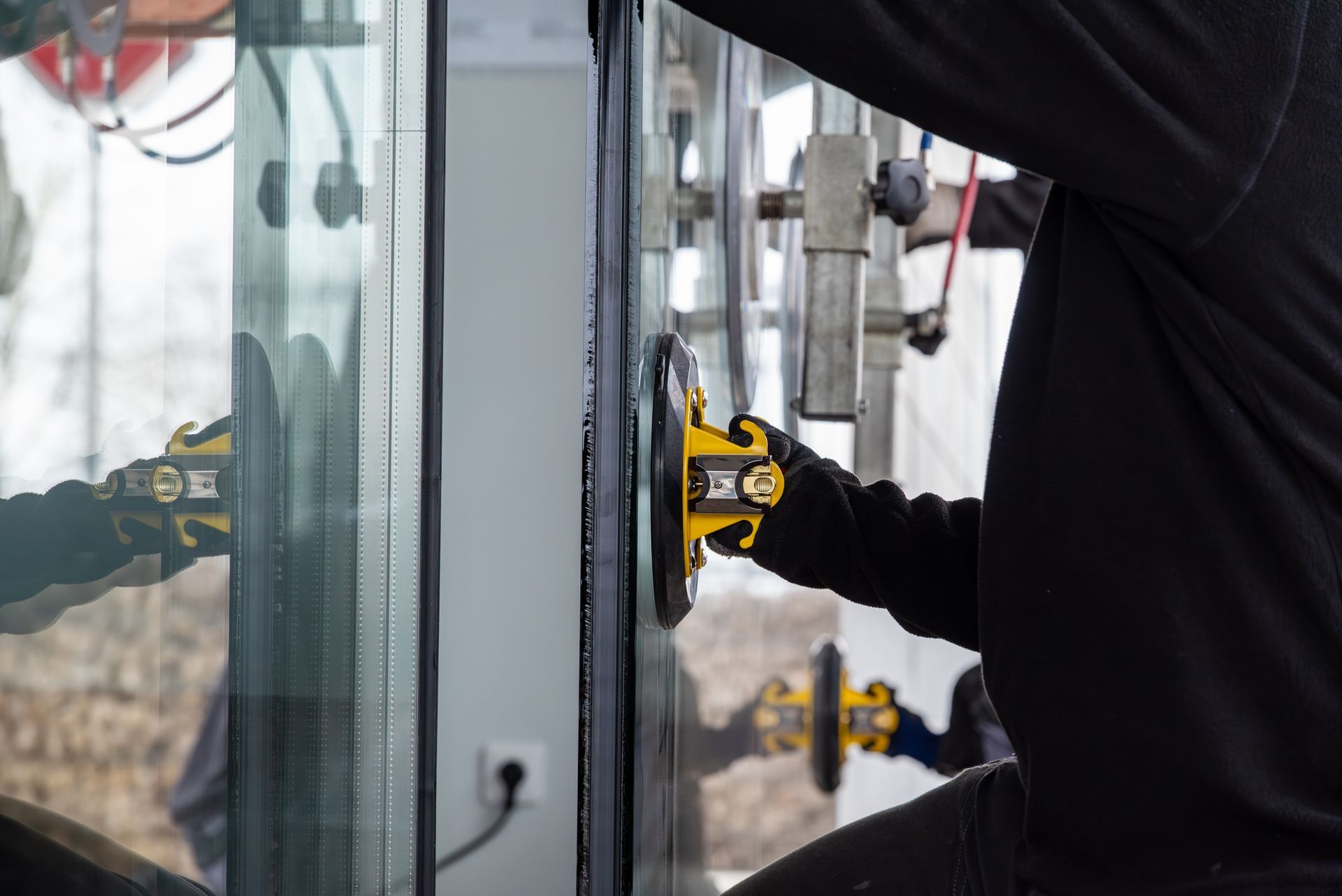 Un ouvrier utilise une ventouse jaune pour installer un grand panneau de verre dans un cadre.