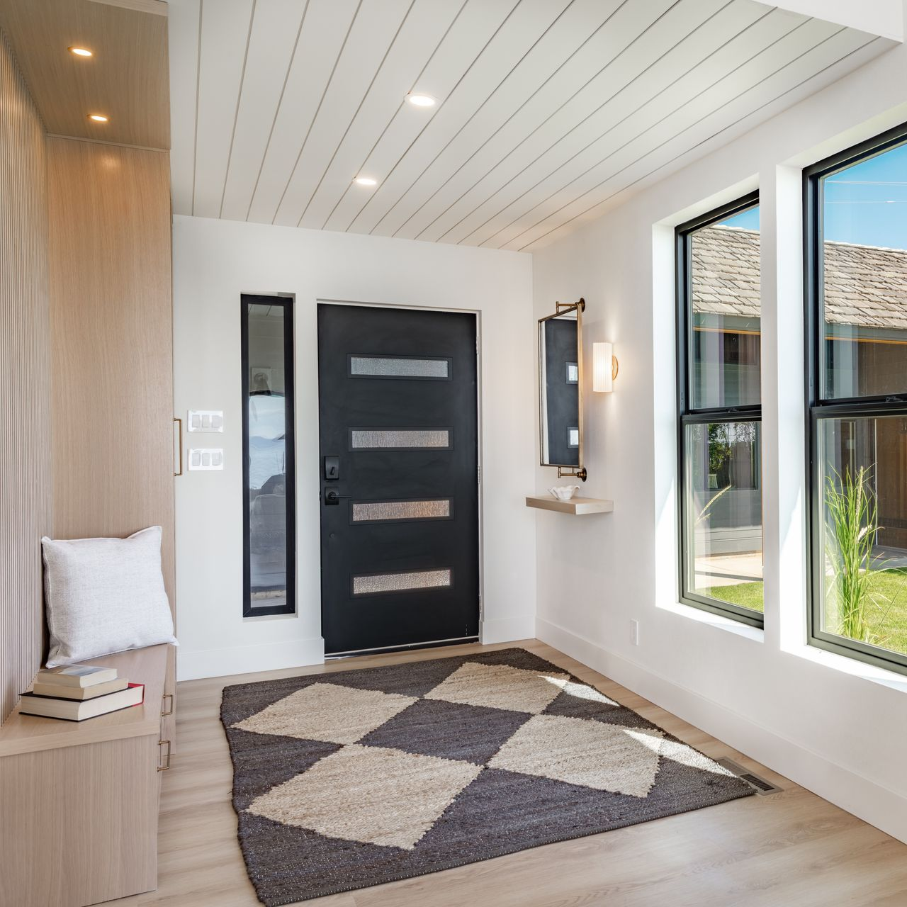 Une entrée moderne avec une porte grise, des murs en bois clair, un plafond lambrissé.