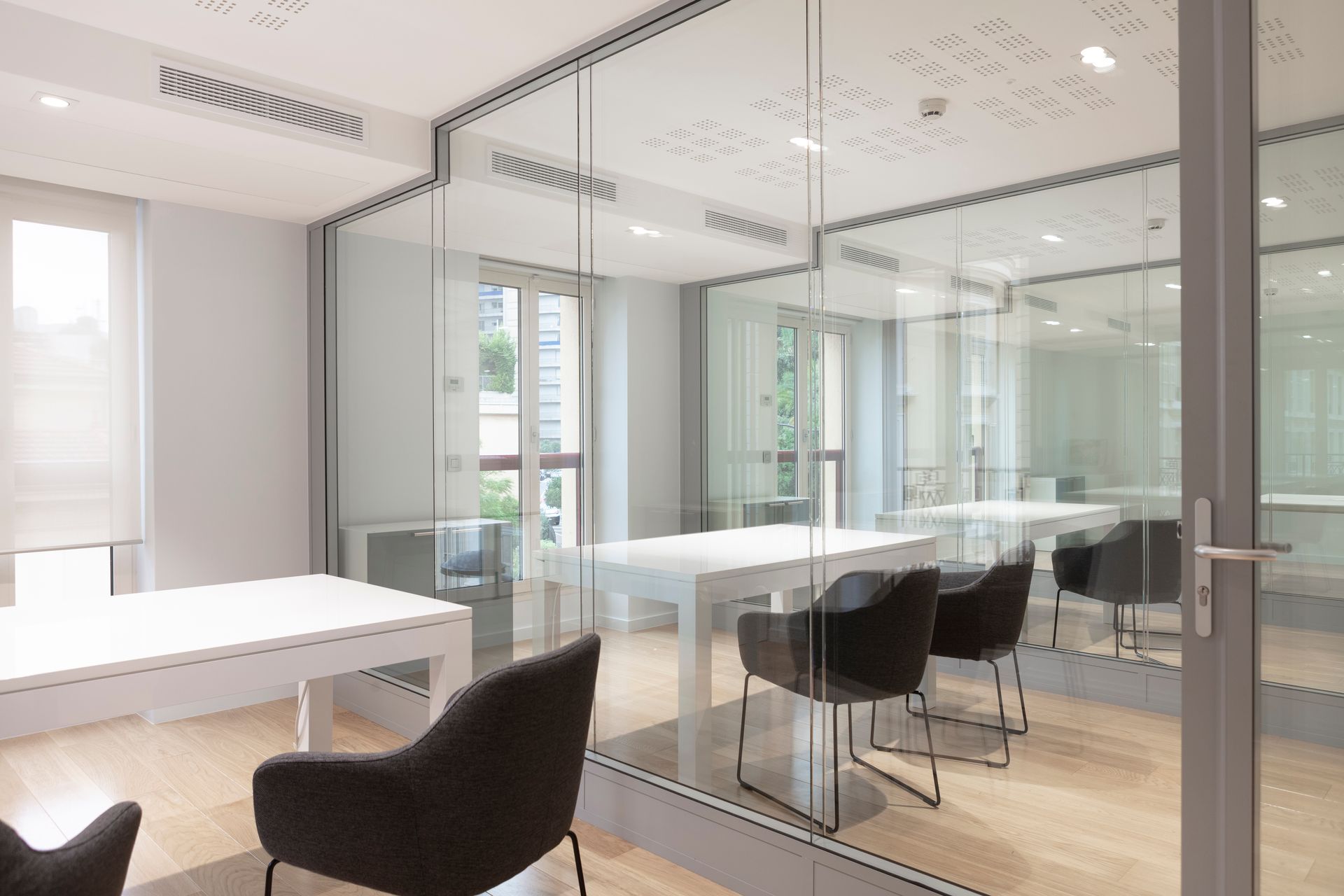 Un espace de bureau lumineux et moderne cloisonné par des parois vitrées sur un parquet clair.