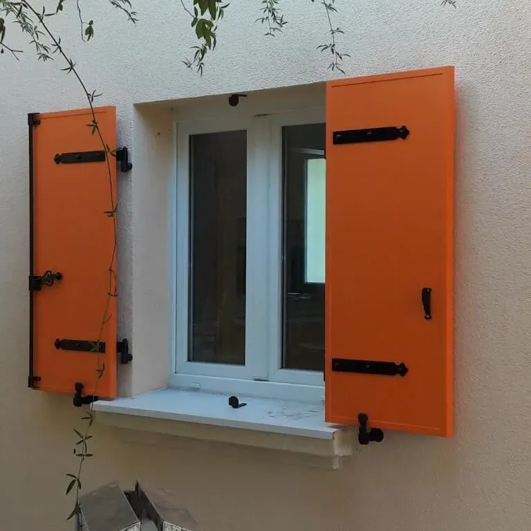 Une fenêtre blanche aux volets orange vif.