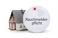 Neben einem Modellhaus steht ein Rauchmelder.