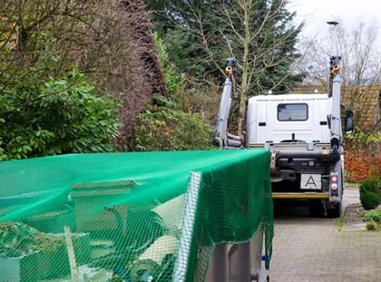 In einer Einfahrt parkt ein Muldenkipper mit einer grünen Plane auf der Ladefläche.