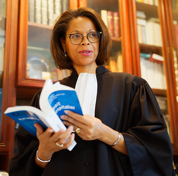 Dans une bibliothèque lambrissée, une personne vêtue d'une robe d'avocat noire traditionnelle et d'un plastron blanc