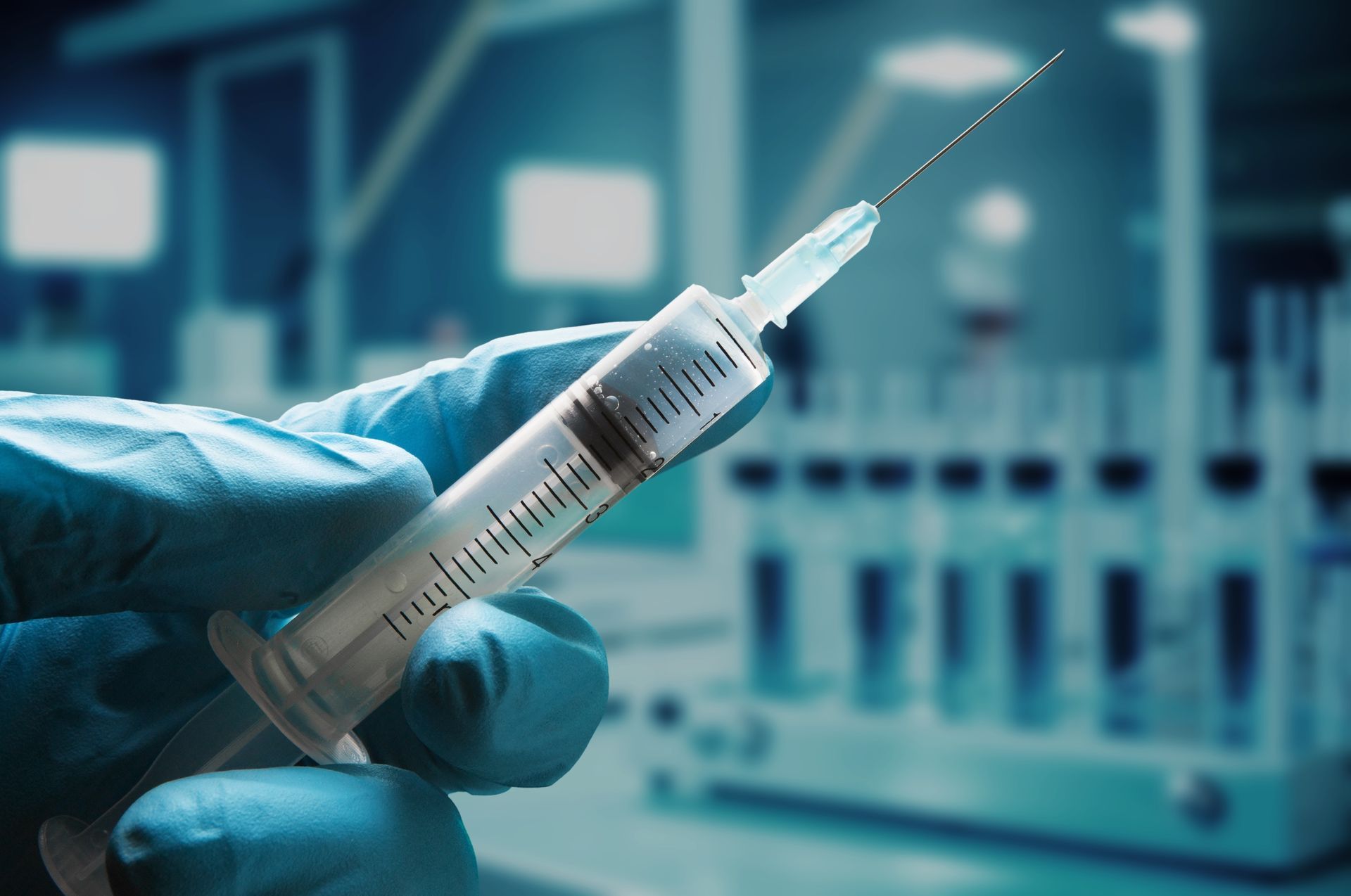 Une main gantée tient une seringue médicale dans un décor de laboratoire flou, avec des tubes à essai en arrière-plan.