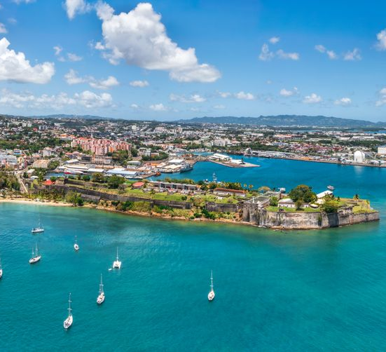 Vue aérienne du fort Saint-Louis, situé sur une pointe côtière, entouré d'eaux turquoise, avec des voiliers