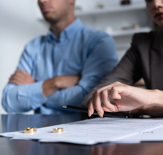 Deux personnes sont assises à une table avec un document légal et deux alliances, symbolisant une réunion de divorce