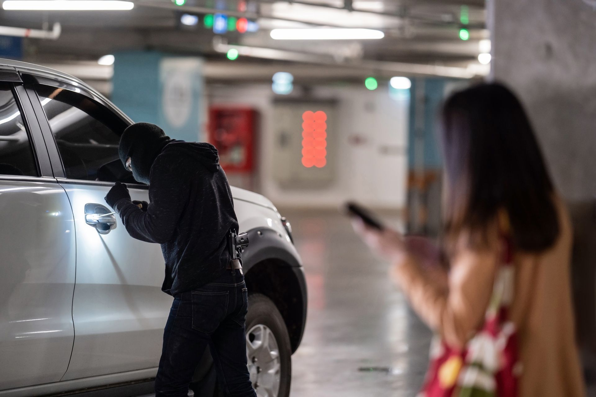 Un individu masqué et vêtu de sombre tente de s'introduire par effraction dans une voiture blanche dans un parking souterrain