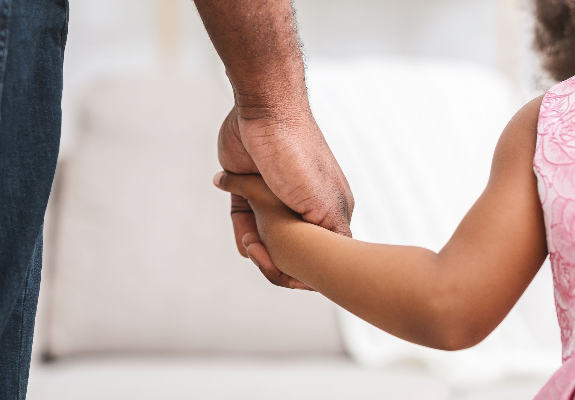 Un adulte tenant la petite main d'un enfant vêtu d'une robe rose.