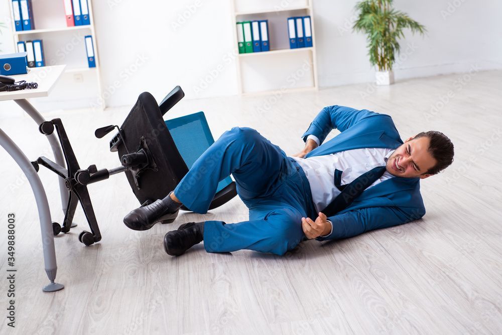 Un homme d'affaires en costume bleu est tombé sur le sol de son bureau, à côté d'une chaise de bureau renversée.