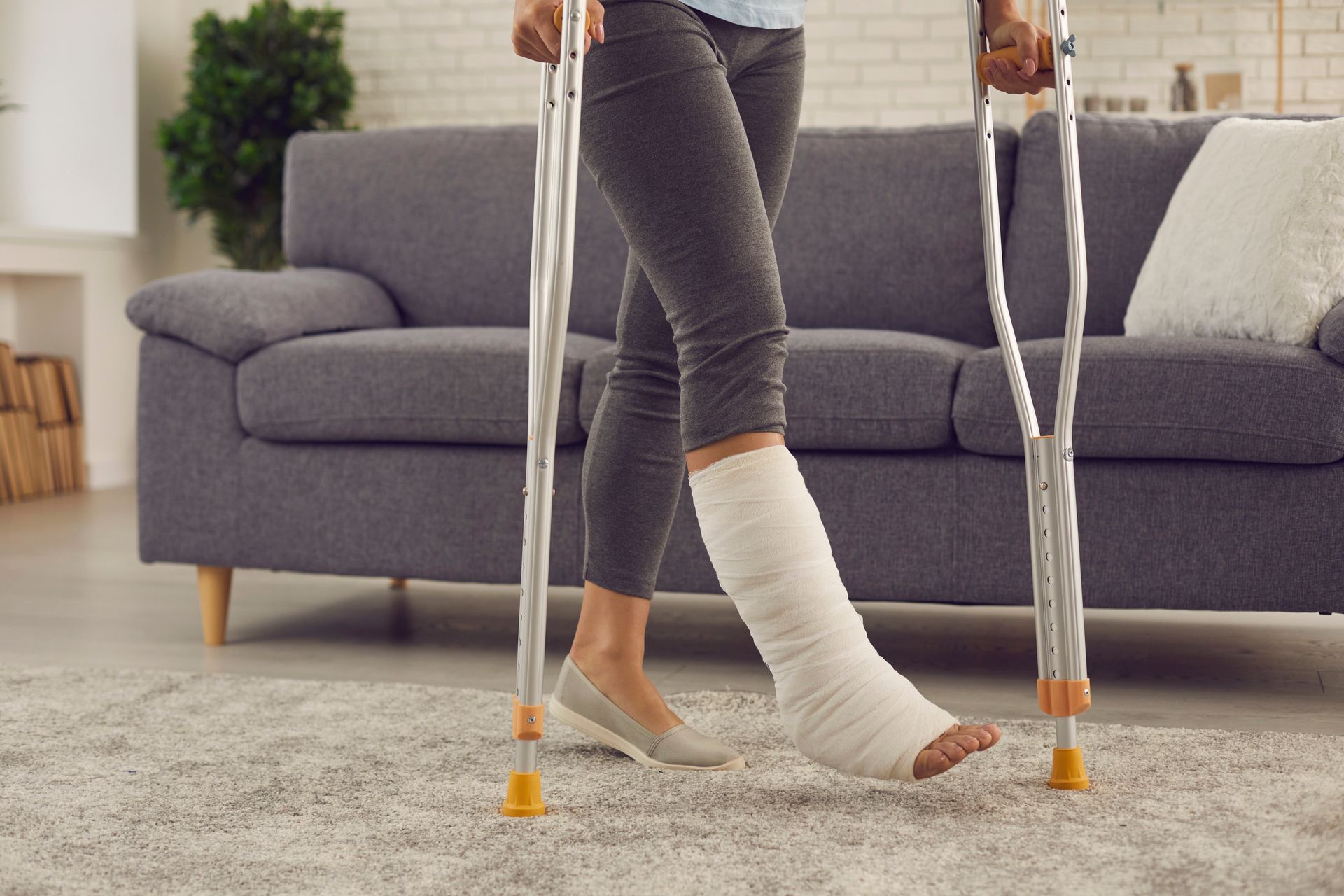 Une personne ayant un plâtre à la jambe se tient debout dans un salon, s'appuyant sur des béquilles.