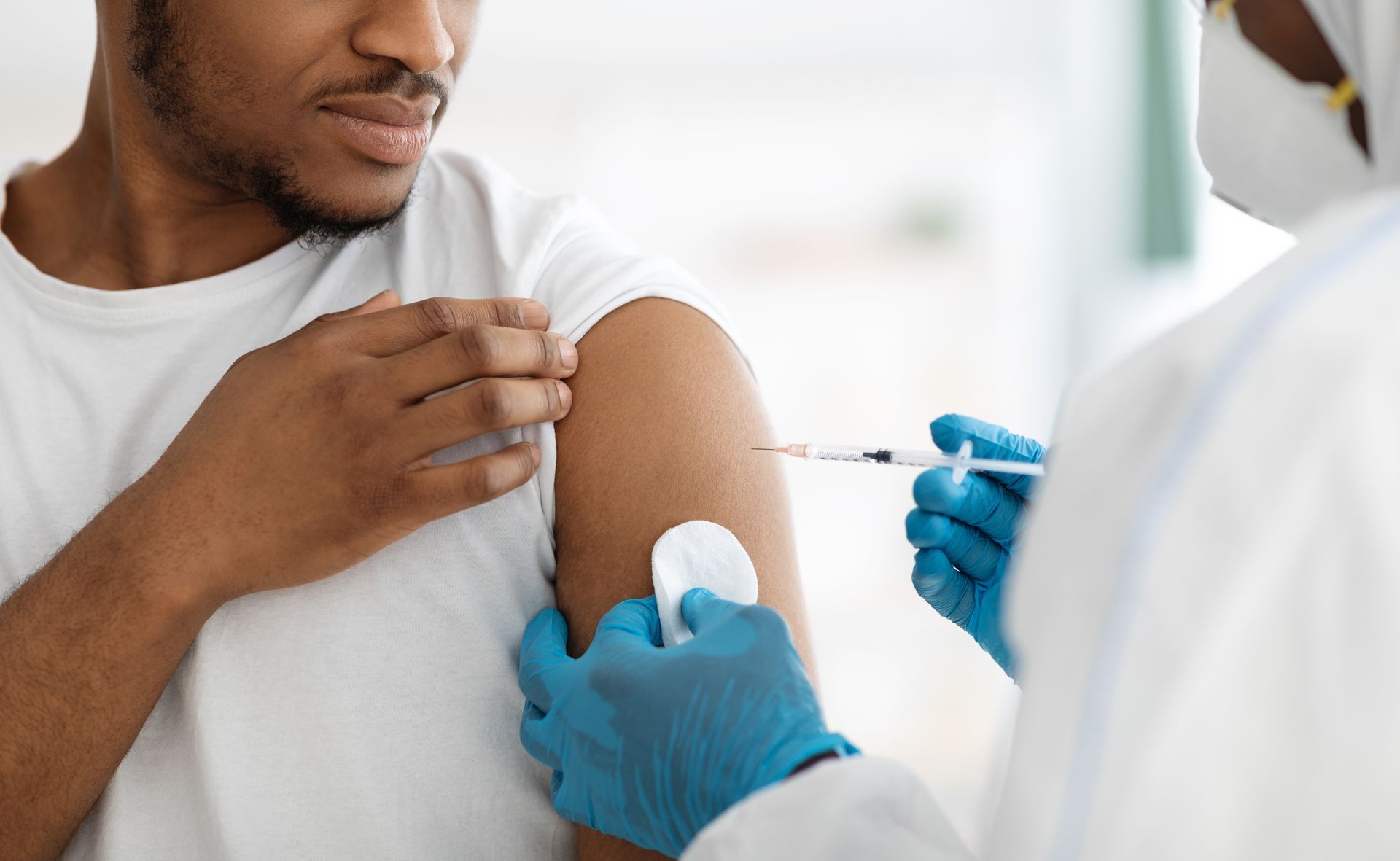 Un agent de santé vêtu d'une blouse blanche et de gants bleus administre une injection dans le haut du bras d'une personne.