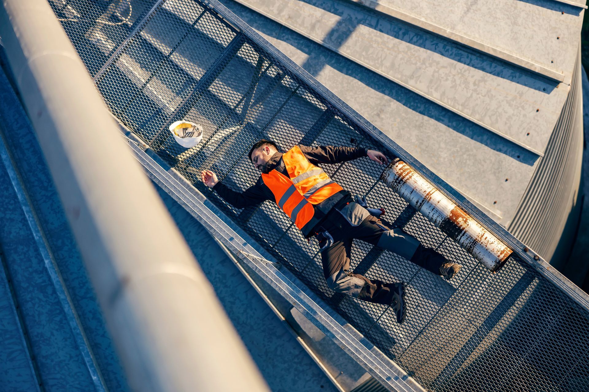 Un ouvrier portant un gilet de sécurité orange est allongé sur une passerelle en caillebotis métallique
