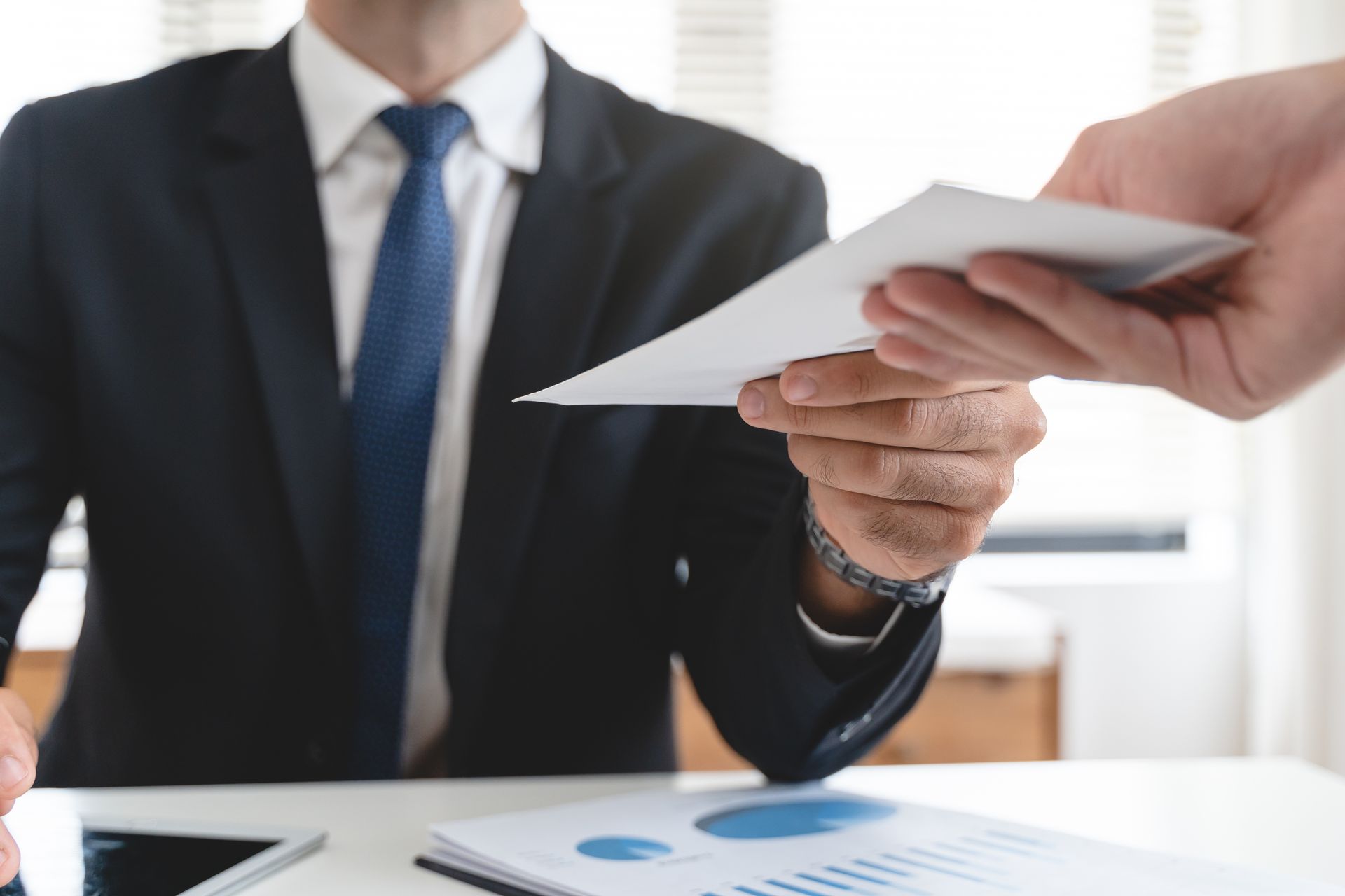 Une personne en costume donne une enveloppe blanche à une autre personne assise de l'autre côté d'un bureau
