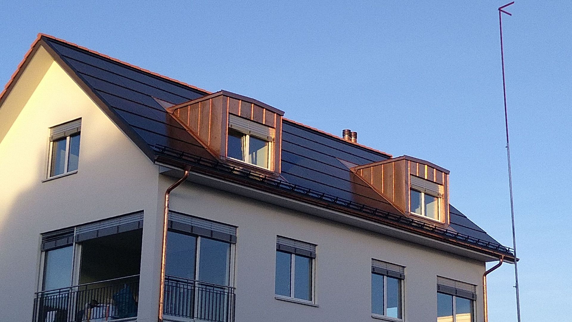 Ein weißes Haus mit einem Kupferbalkon und einer Kupferdachrinne