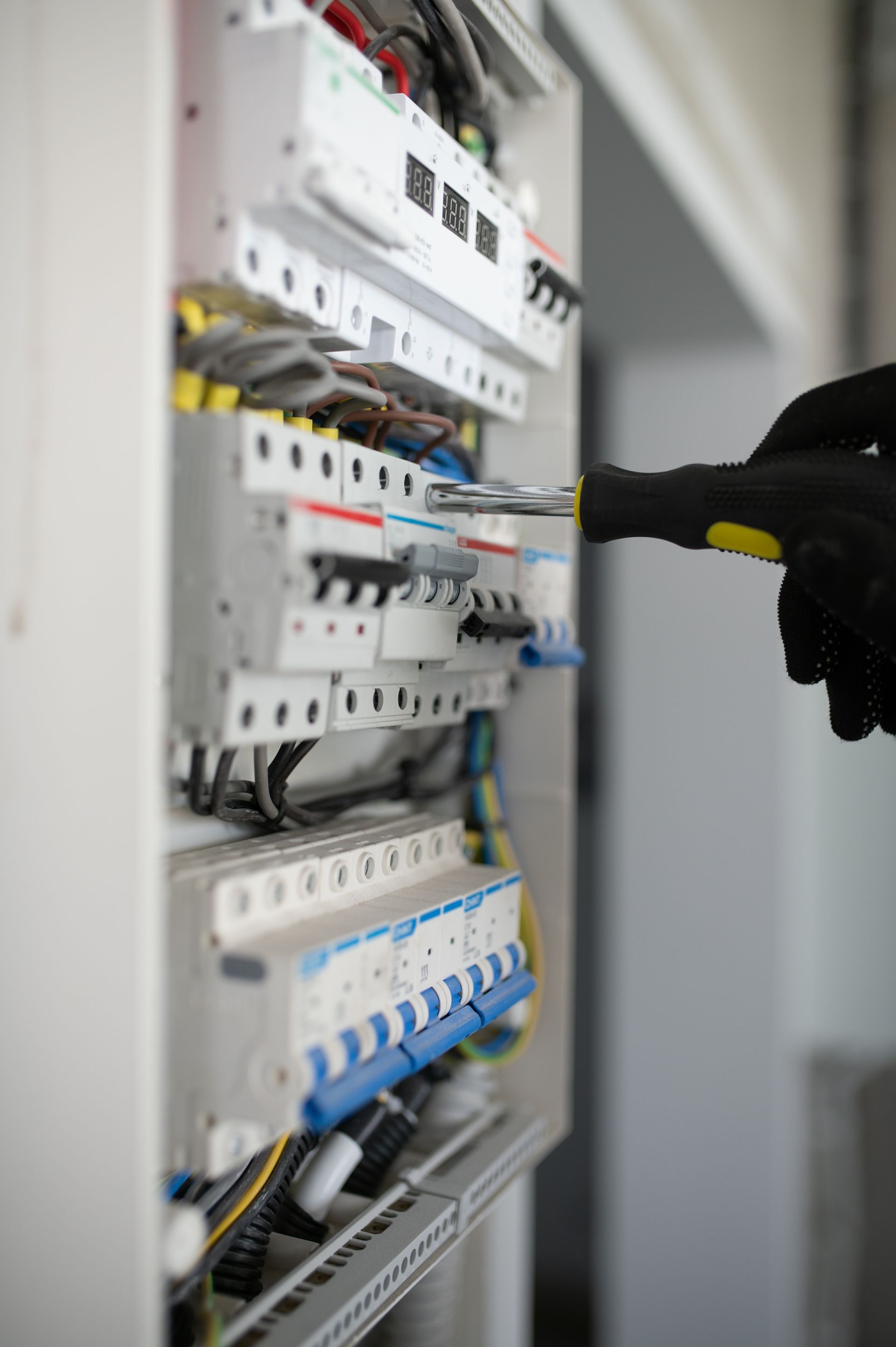 Main gantée d'un électricien utilisant un tournevis sur un tableau électrique.