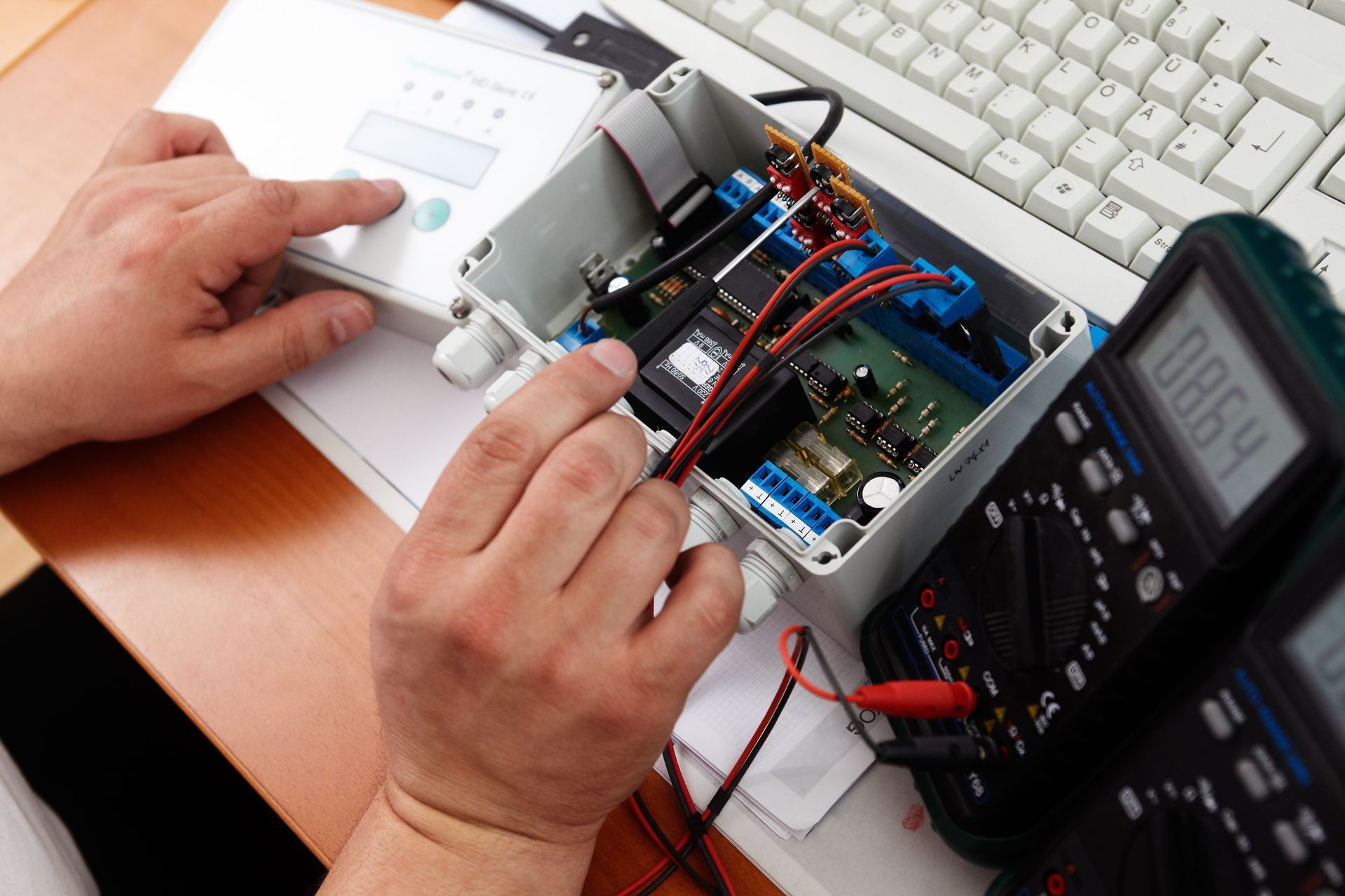 Une personne teste un appareil électronique dont le câblage est ouvert à l'aide de multimètres.