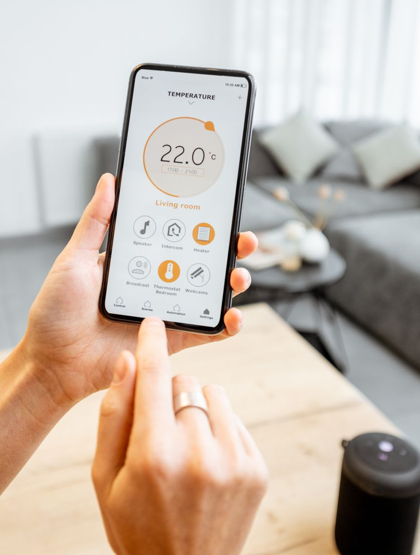 Une personne tenant un téléphone affichant une application domotique de contrôle de la température, à l'intérieur.