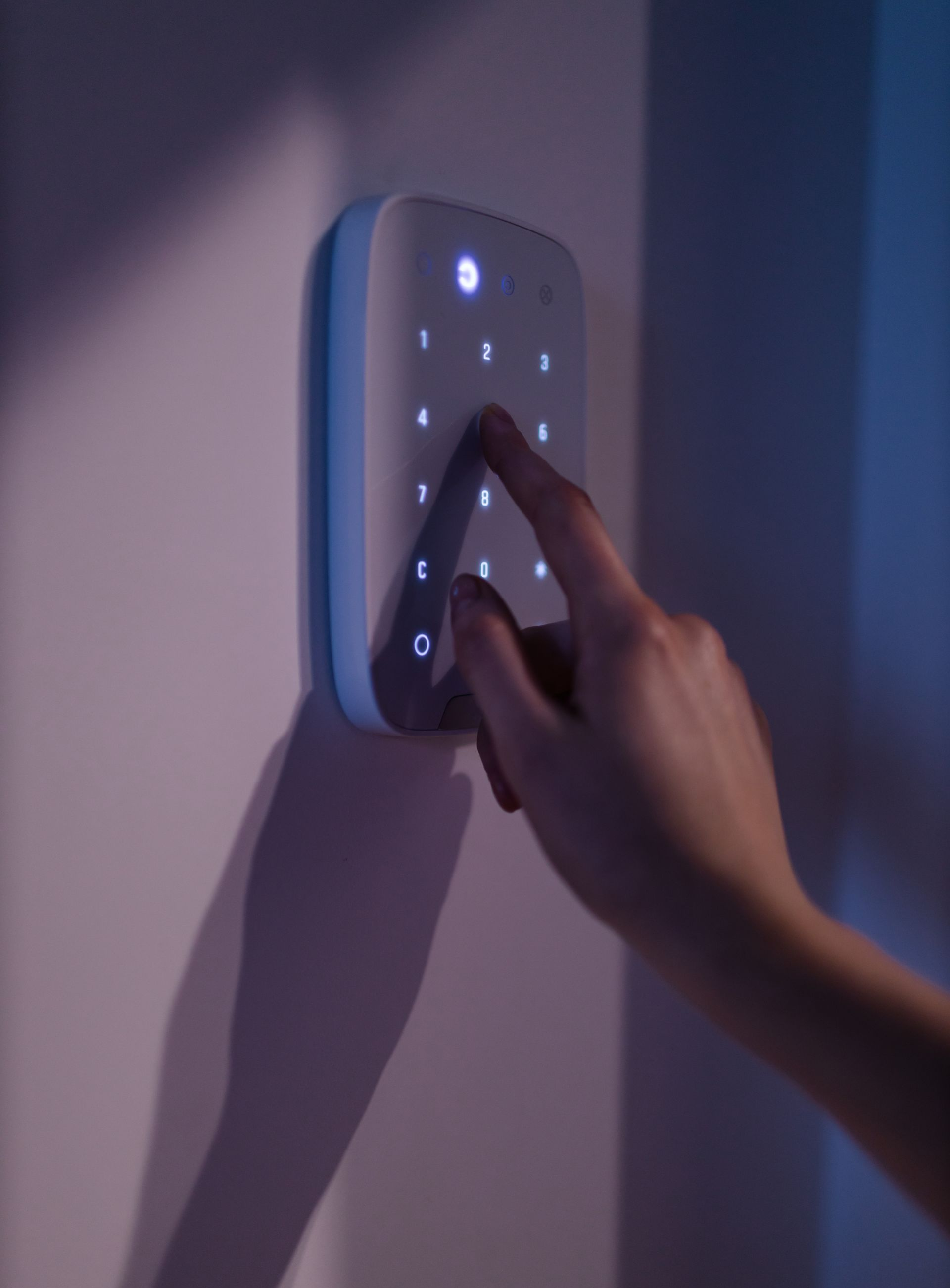 Saisie manuelle d'un code sur un clavier de système de sécurité, fixé sur un mur blanc.