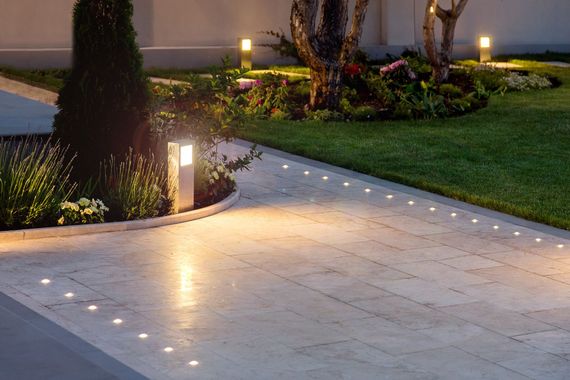 Allée éclairée par des spots intégrés, bordée de pelouse et de jardin, avec éclairage indirect.