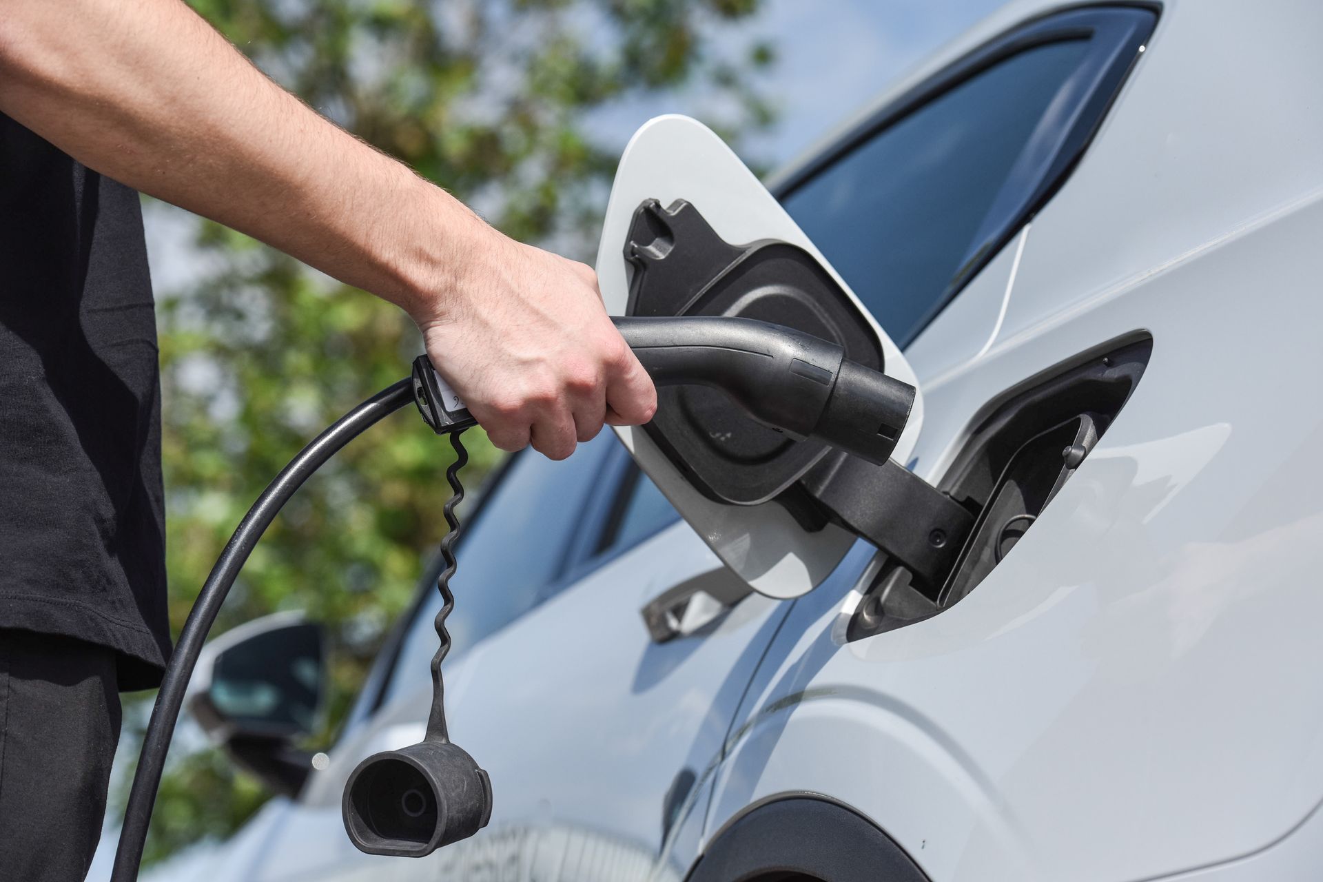 Une main branche un câble de recharge à une voiture électrique blanche, au niveau d'une prise de recharge.