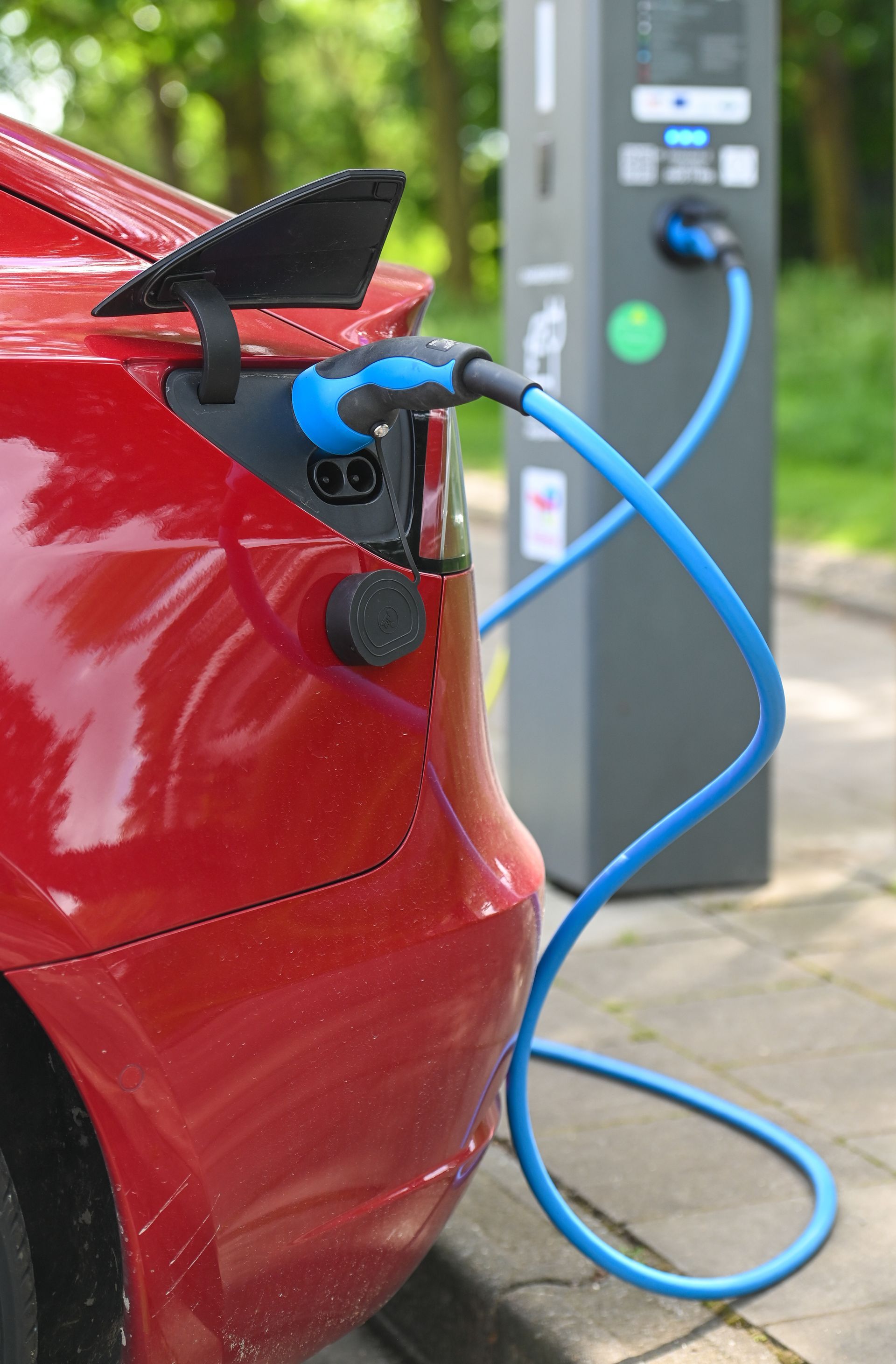 Voiture électrique rouge branchée à une borne de recharge avec un câble bleu.