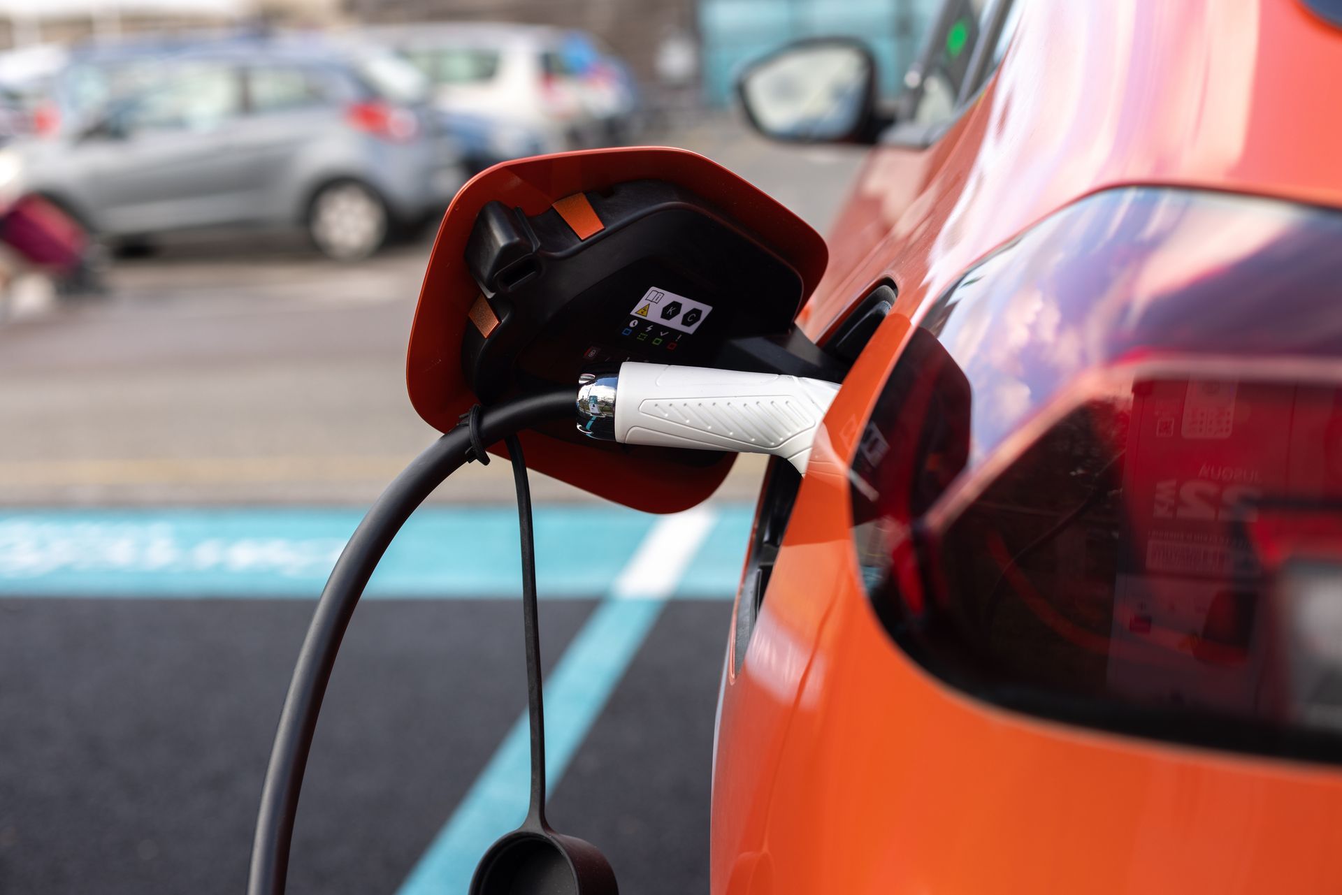 Voiture électrique orange branchée à une borne de recharge extérieure.