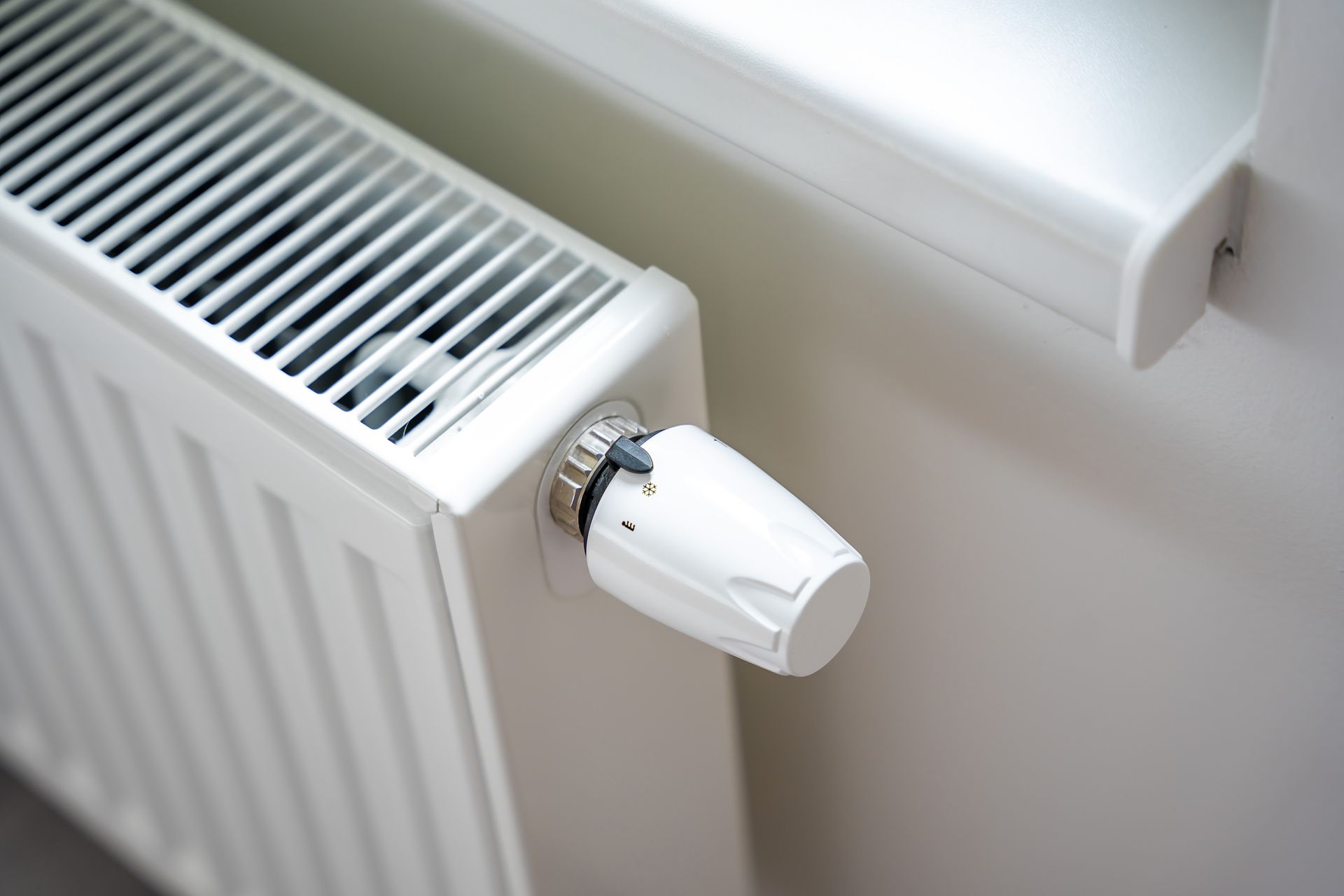 Radiateur blanc avec bouton de thermostat près d'une fenêtre.