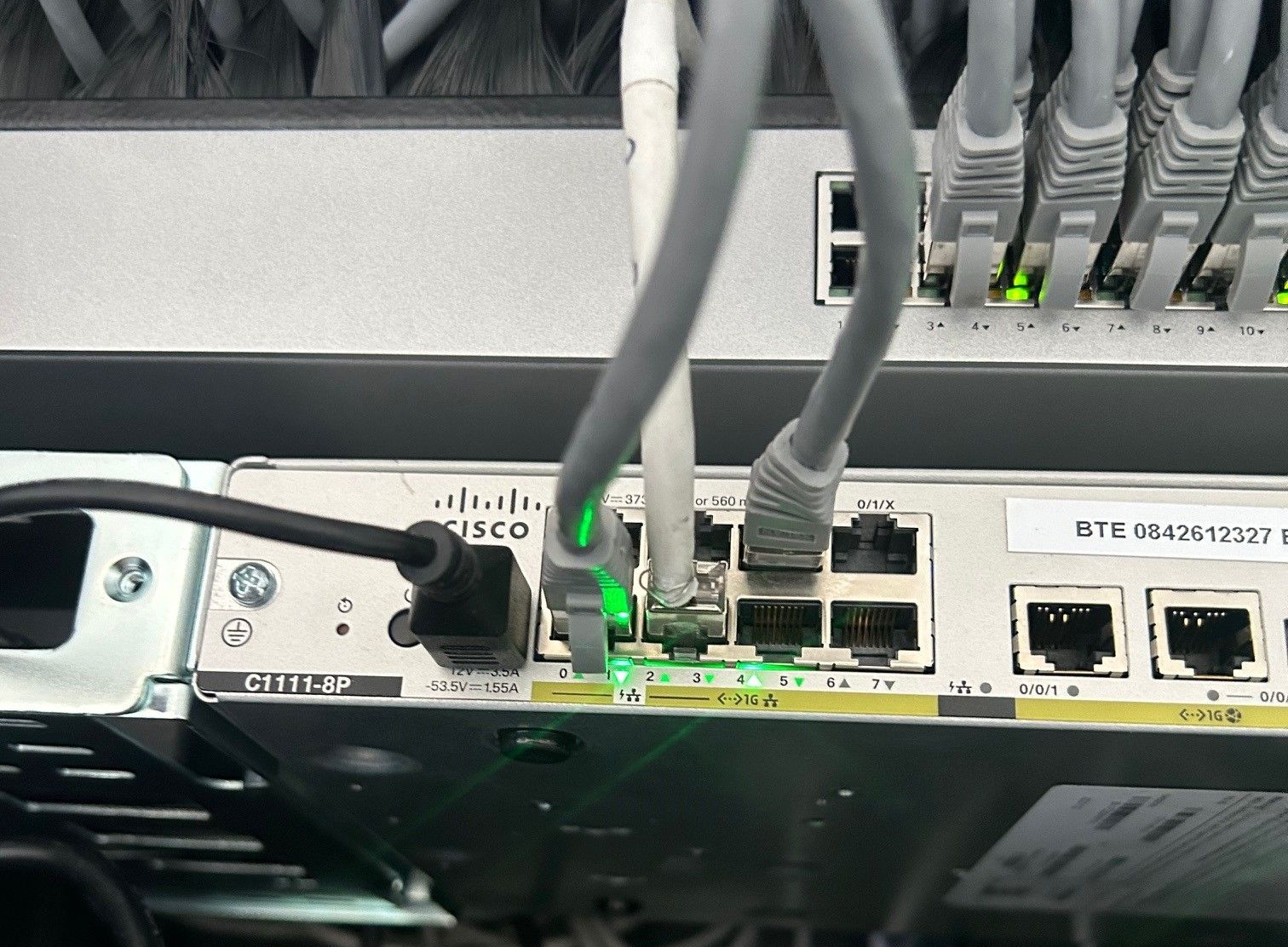 Gros plan sur un commutateur réseau Cisco avec plusieurs câbles Ethernet branchés. Des ports ont des voyants verts, indiquant des connexions actives.