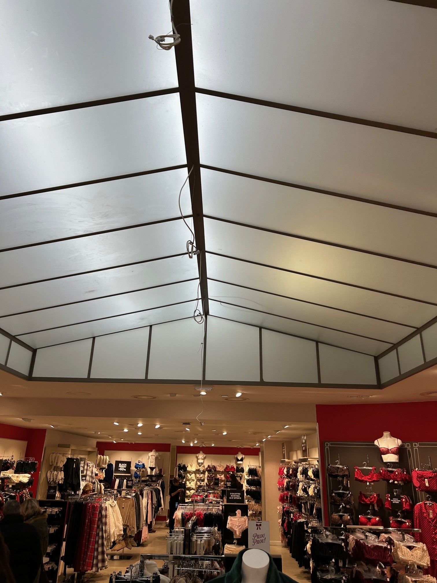Vue intérieure d'un magasin de vêtements avec un haut plafond blanc en pente et des présentoirs de marchandises.