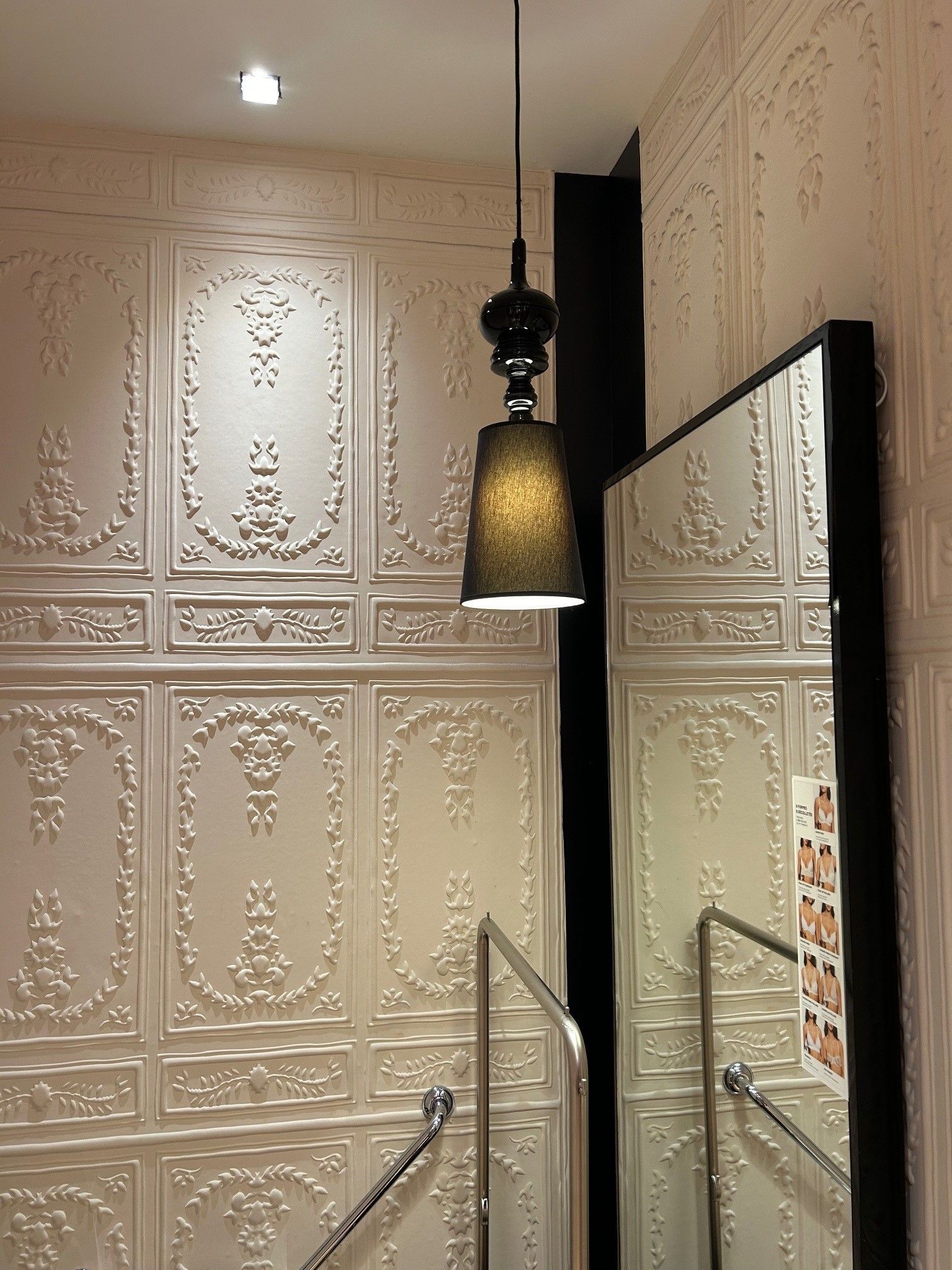 Une pièce ornée de boiseries blanches, d'un luminaire suspendu noir et d'un grand miroir.