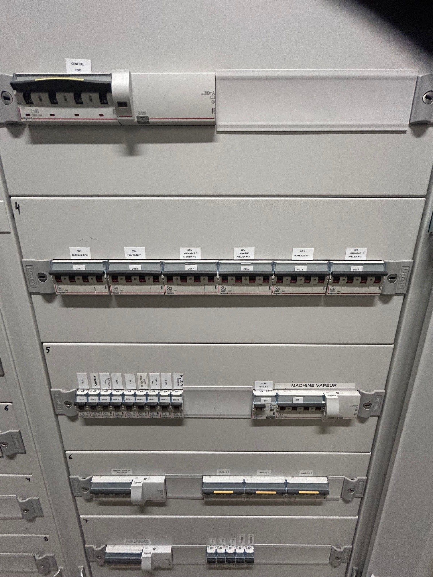 Tableau électrique avec plusieurs disjoncteurs et étiquettes. Métal gris.